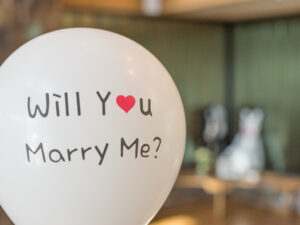 Luftballon mit dem Aufdruck „Will You Marry Me“ vor unscharfem Hintergrund